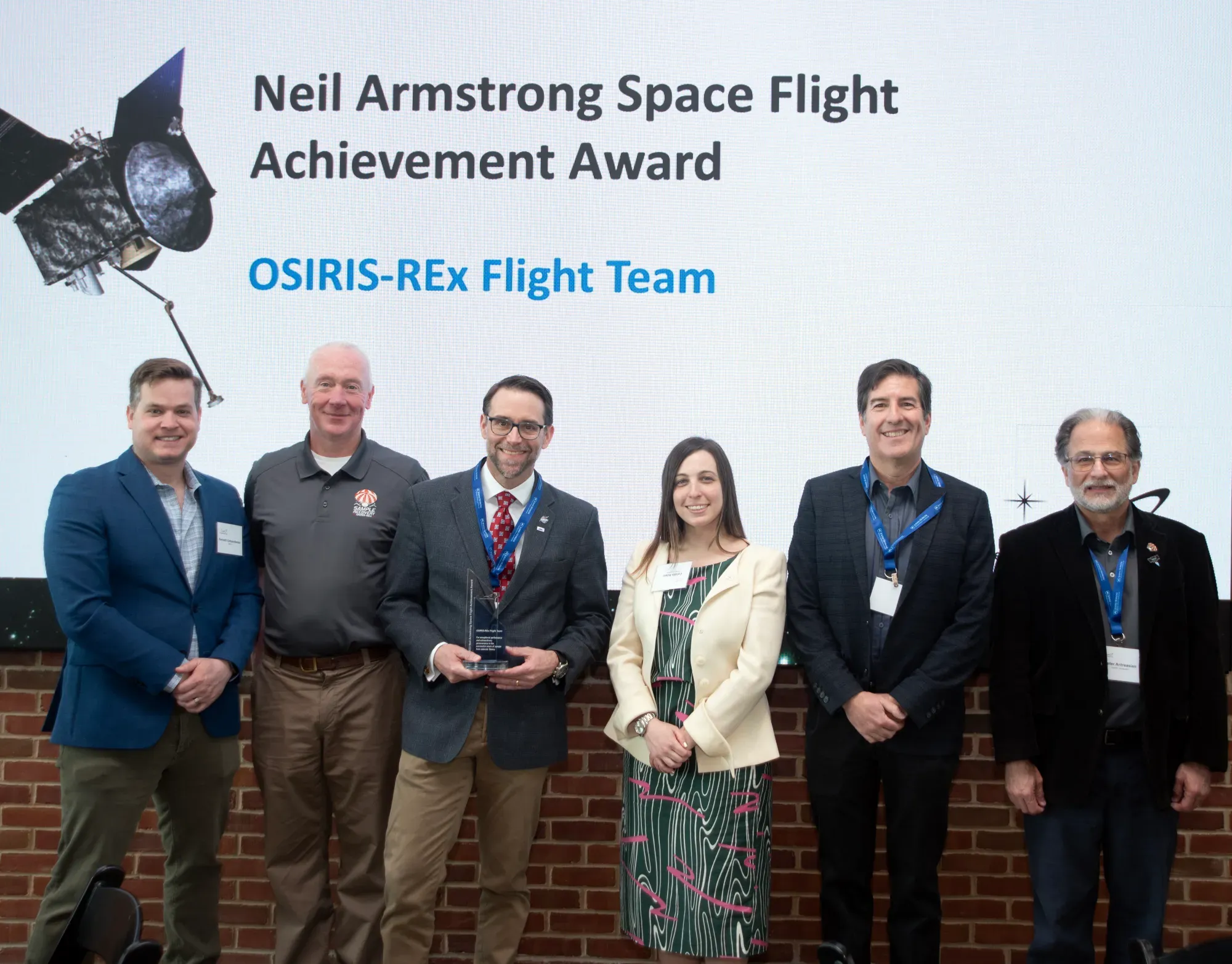 team holds award and stands in front of sign that reads Neil Armstrong Space Flight Achievement Award: OSIRIS-REx Flight Team