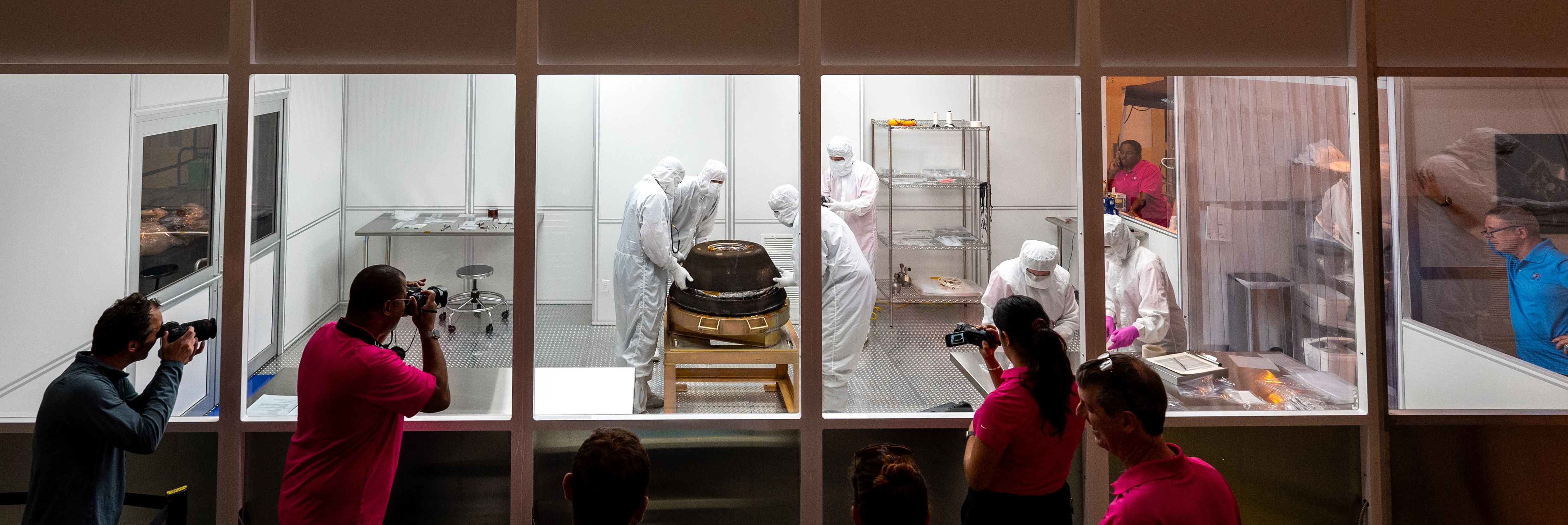 people look through windows and take pictures of the capsule being opened in a clean room